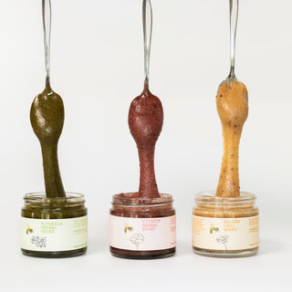 Three jars of honey with spoons filled with honey dripping back into the jars on a white background.